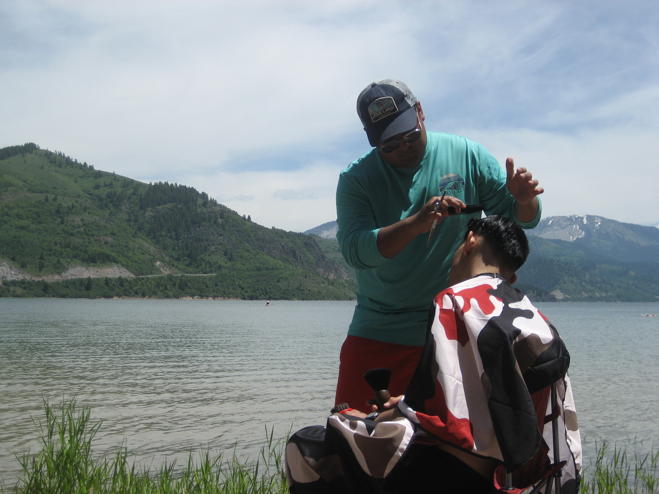 Carlos cutting hair by the lake with mountain scenery